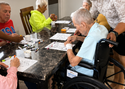 Male and female residents and a caregiver participating in a group coloring and art activity at a dining table at Paradise Manor assisted living facility in Florida