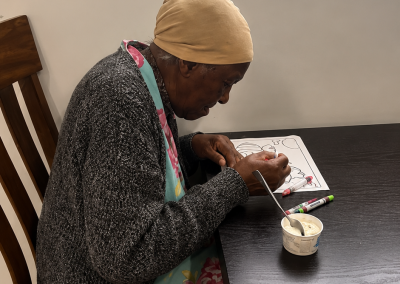 Elderly resident seated at a table concentrating on a coloring activity with markers at Paradise Manor Florida ALF