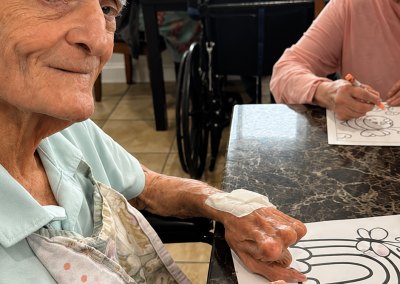 Elderly male resident smiling warmly while participating in a rainbow coloring activity at Paradise Manor assisted living facility in Florida with other residents visible in background