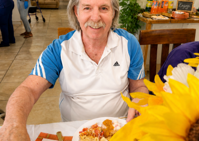 Happy male resident smiling at a holiday meal in a Florida assisted living home dining area with sunflowers and beverages