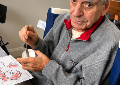 Elderly male resident in a wheelchair participating in a coloring art activity with a snack at Paradise Manor male-only assisted living facility in Florida